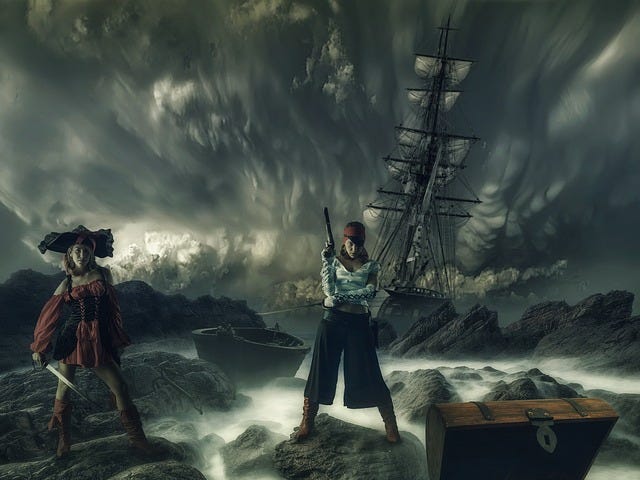 Women dressed as pirates standing or rocks, treasure chest in the foreground, ship and storm clouds in the background