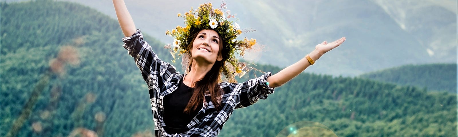 girl with long brown hair wearing wreath of flower on her head waling through grassy field with hands upraised