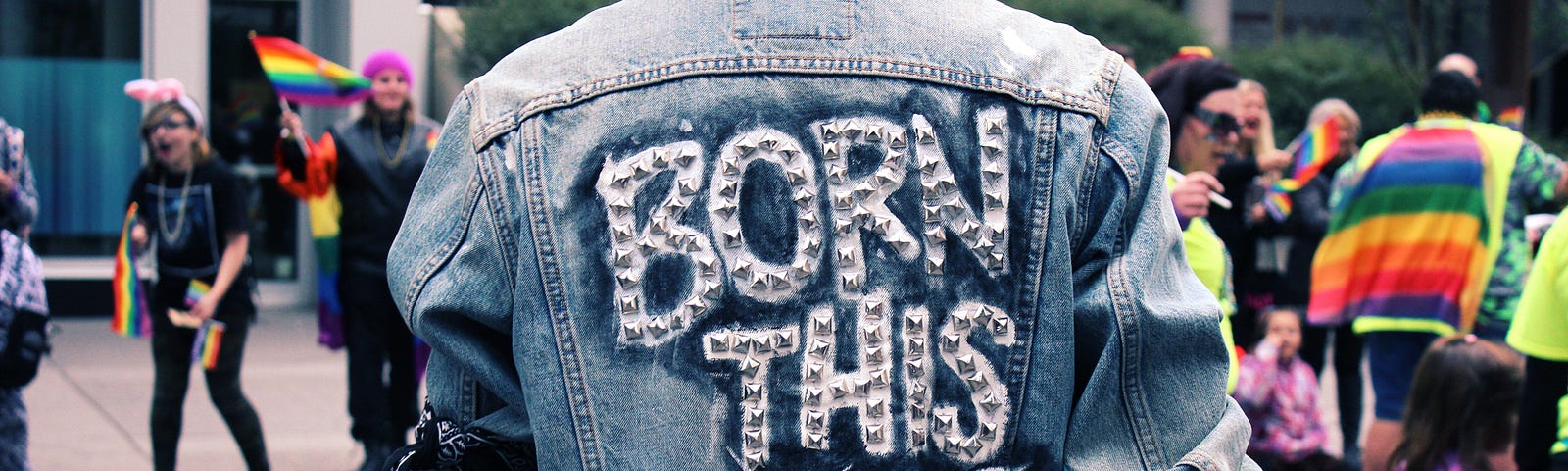 Man at a Pride parade wearing a denim jacket that says “Born This Way”