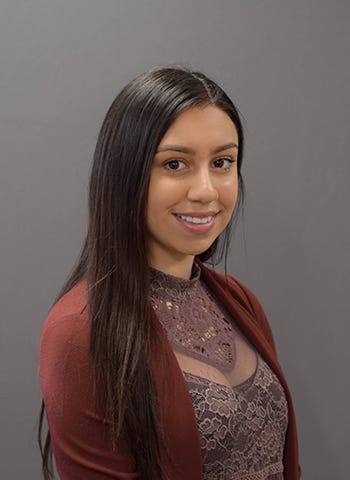 Aurora Sanchez is pictured wearing a mauve cardigan against a gray background