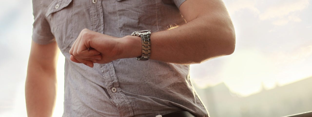 Image of a man’s torso, focused on his arm positioned so that he can see his watch, checking the time.