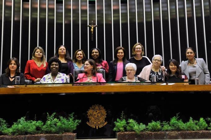 Foto de uma bancada no Congresso Nacional Brasileiro contendo 13 deputadas federais de diferentes partidos que foram eleitas.
