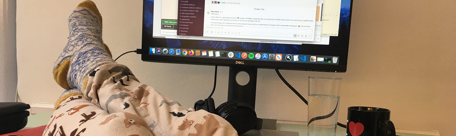 Feet up on a desk, wearing pyjama bottoms, keyboard on lap and Slack on screen.