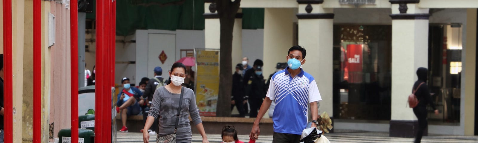 A couple and their child walk down the street, wearing masks and holding hands