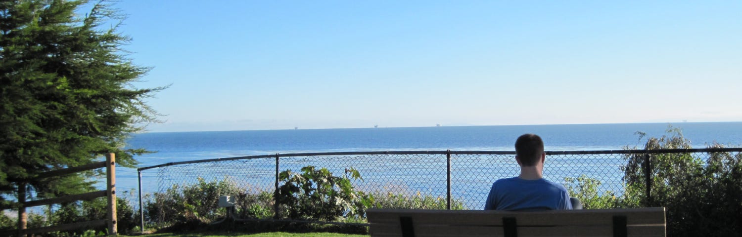 Man sitting on bench in Summerland, California, gazing thoughtfully at ocean