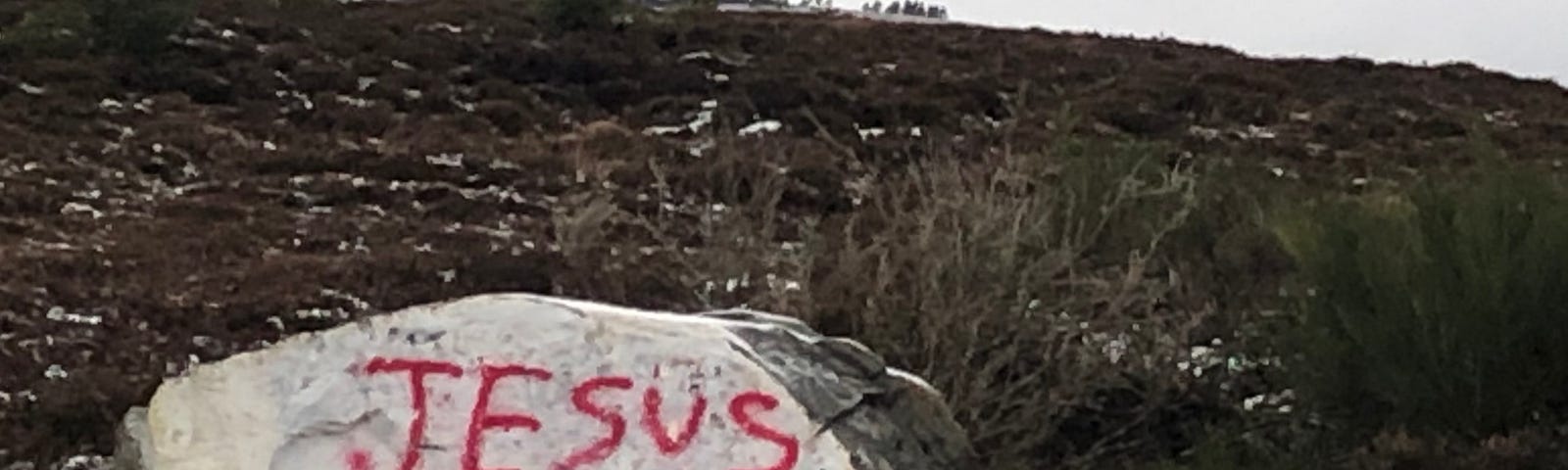 A large boulder on moorland, with one side painted white and the words “Jesus Saves” spray painted in red