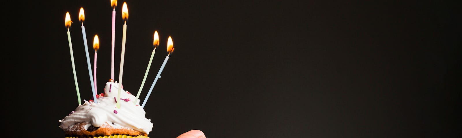 hand holding iced cupcake with many birthday candles