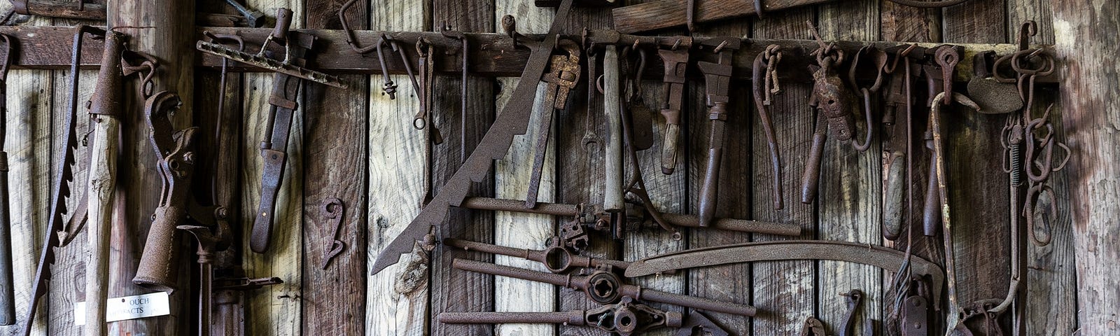 An image of rustic tools organised on a wall with a work bench underneath