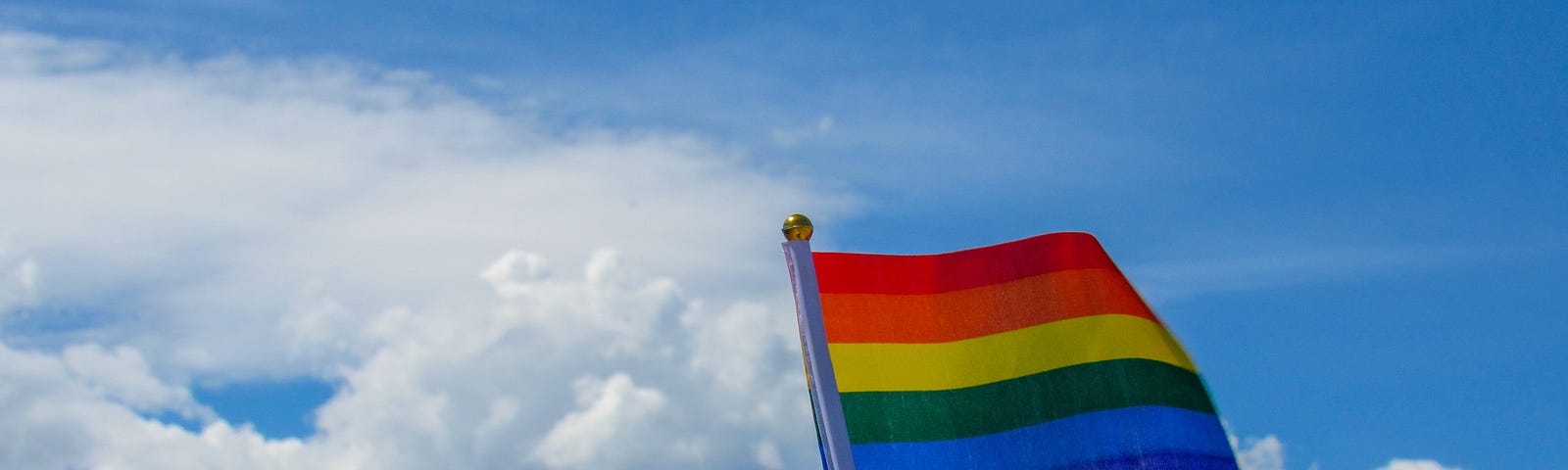 Rainbow flag waving in front of the sky
