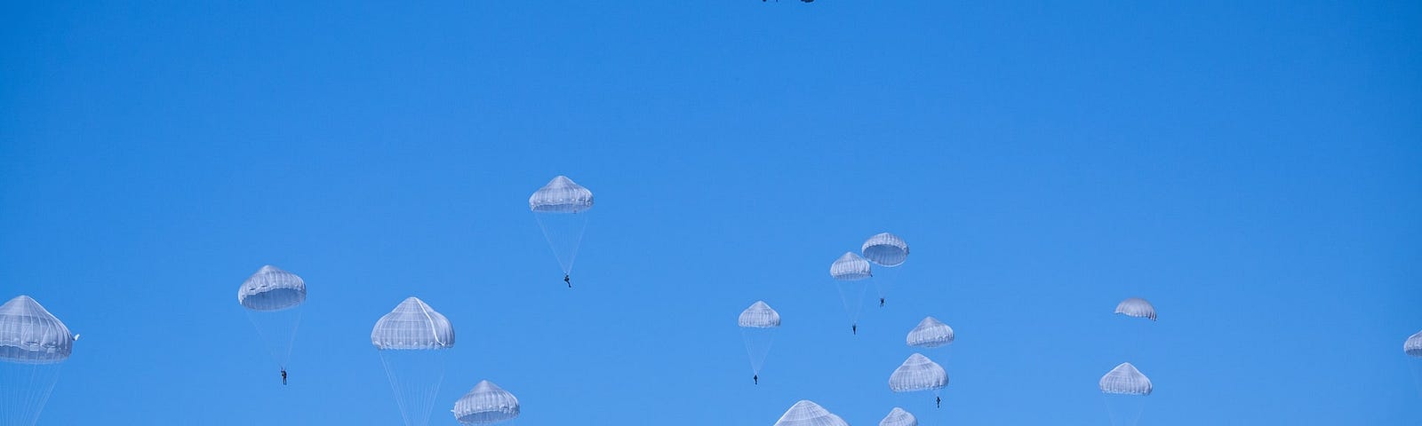 Parachutists drop from a distant plane against clear blue sky.