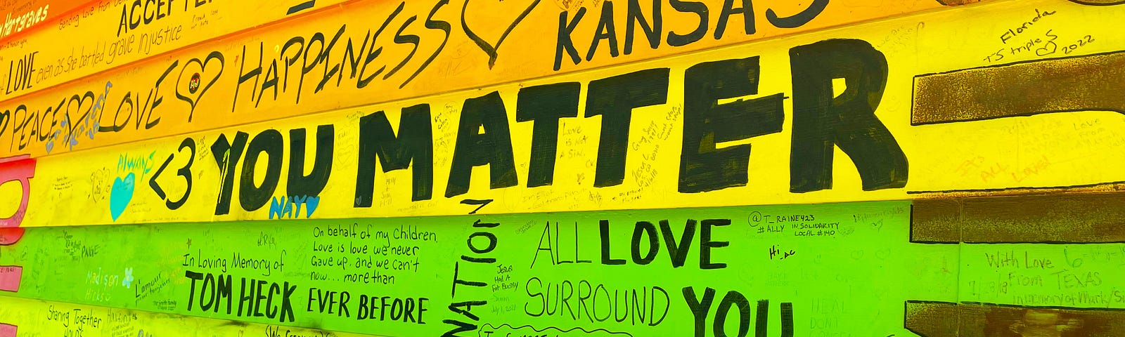 A house wall is painted rainbow colors with several loving messages on it. The largest and most important one says “You matter”.