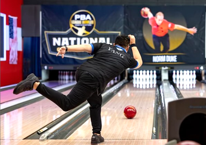 A professional bowler attempts to get a strike in a tour event as he just released his maroon ball down the lane.