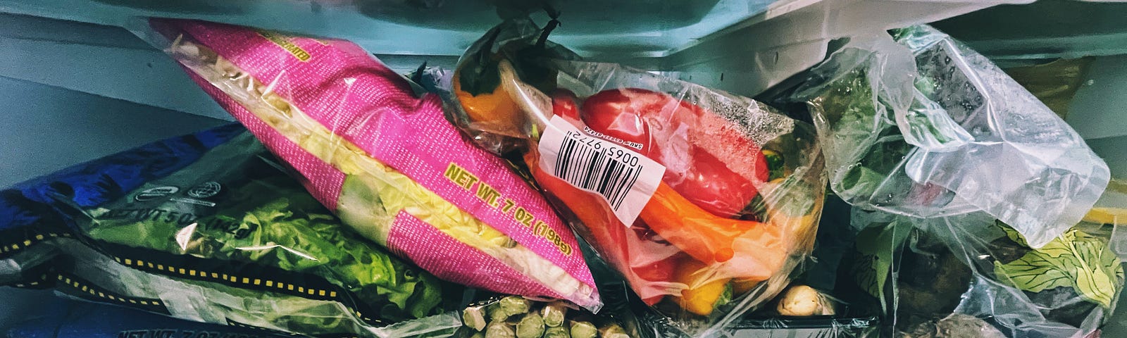 Vegetables packaged in plastic bags, stacked in a fridge shelf.