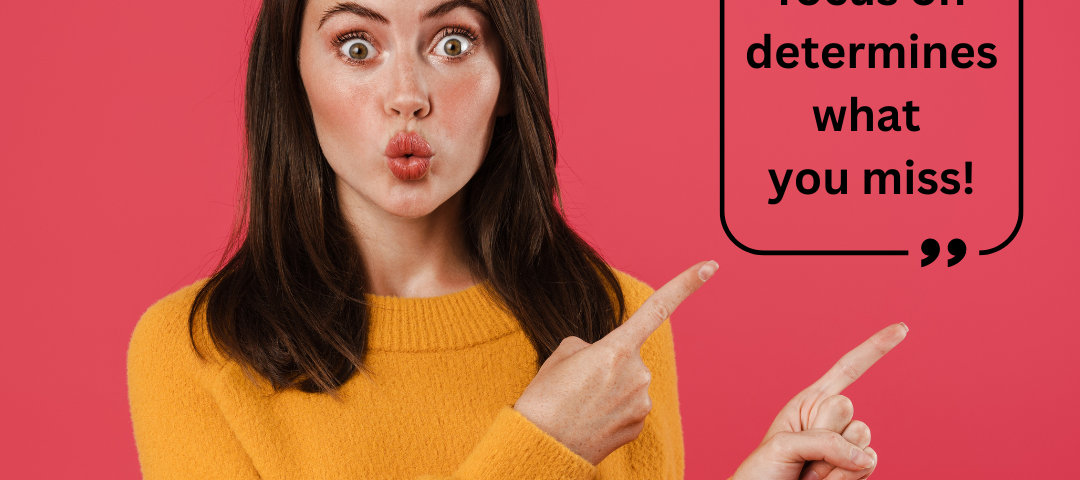 a woman wearing a yellow sweater standing in front of a red background- pointing to a sign that says “what you focus on determines what you miss.”