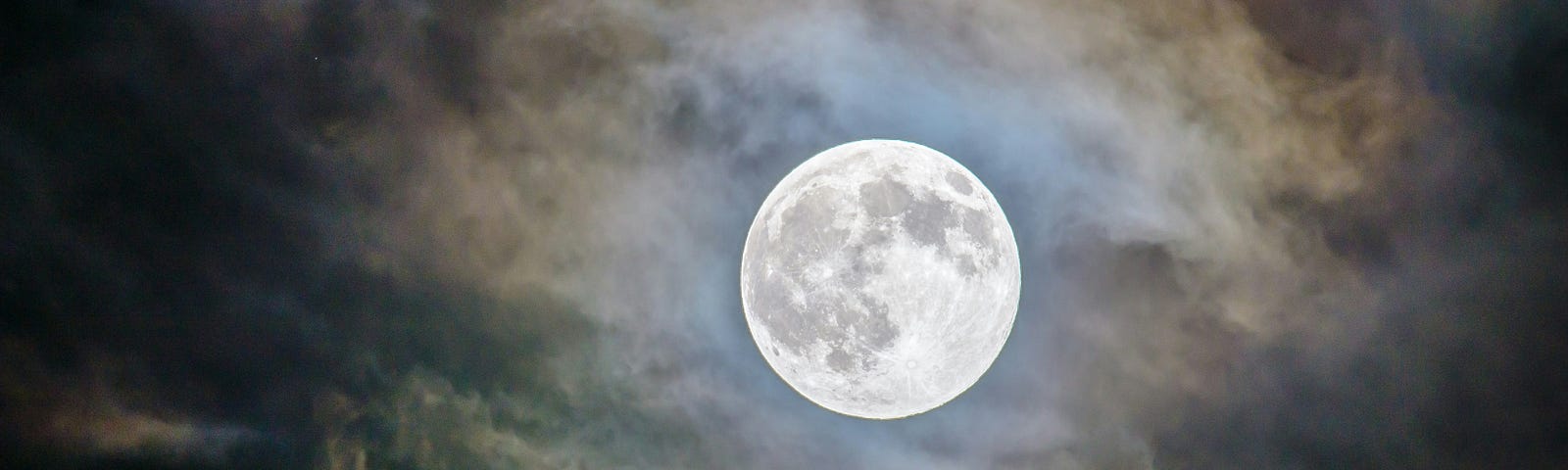 A full moon looks ominous in a cloudy night sky as it breaks through the clouds illuminating its surface.