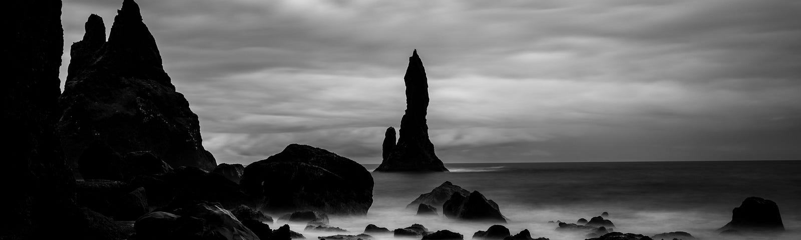 Monochromatic, gloomy beach scene with looming black rocks and smoky blur of water