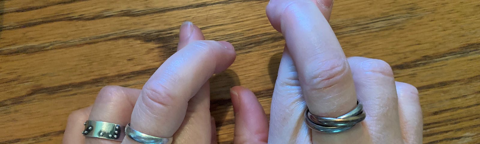 Two Caucasian hands side by side with crossed fingers on each hand.