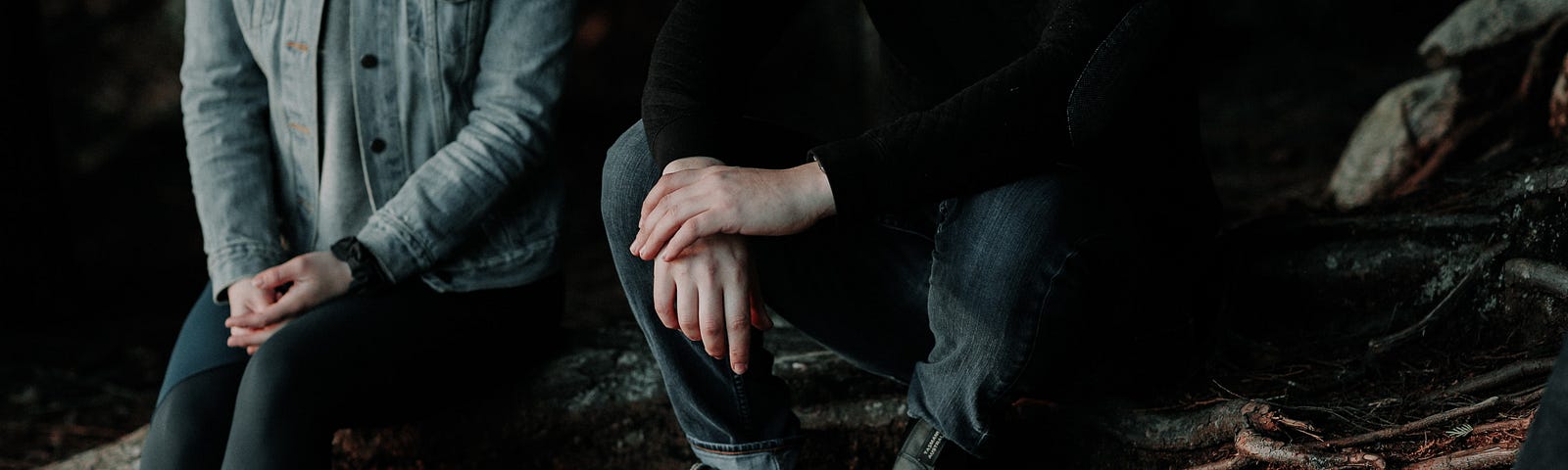 Man and woman sitting apart (in a forest) on tree roots holding their own hands and not each others’.