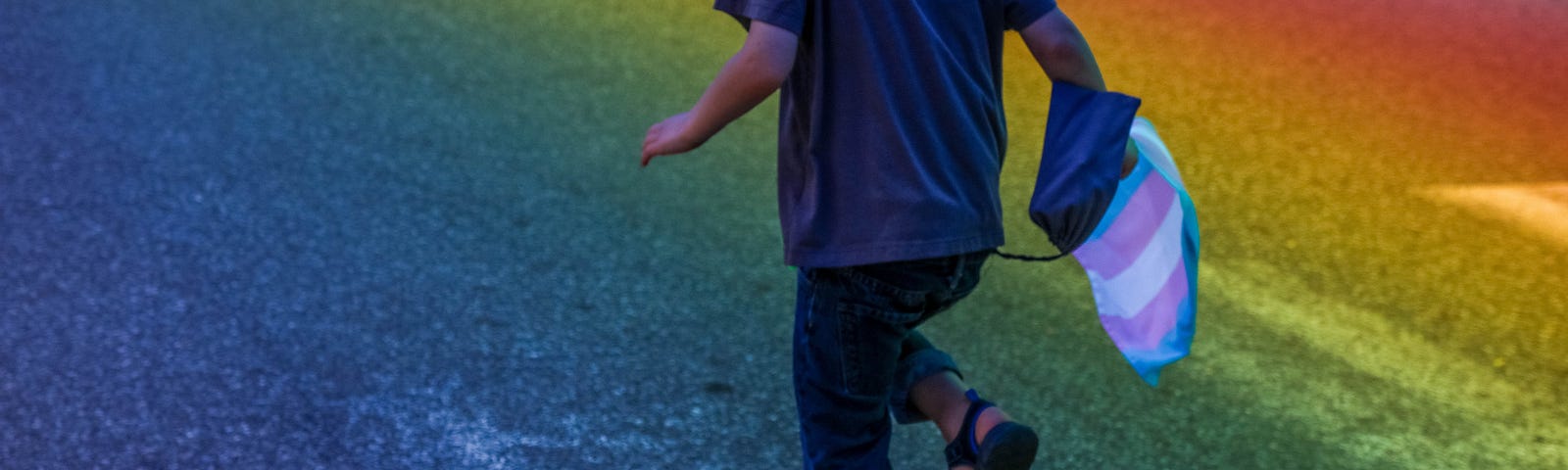 child running through a grassy field with a Trans flag in their hand