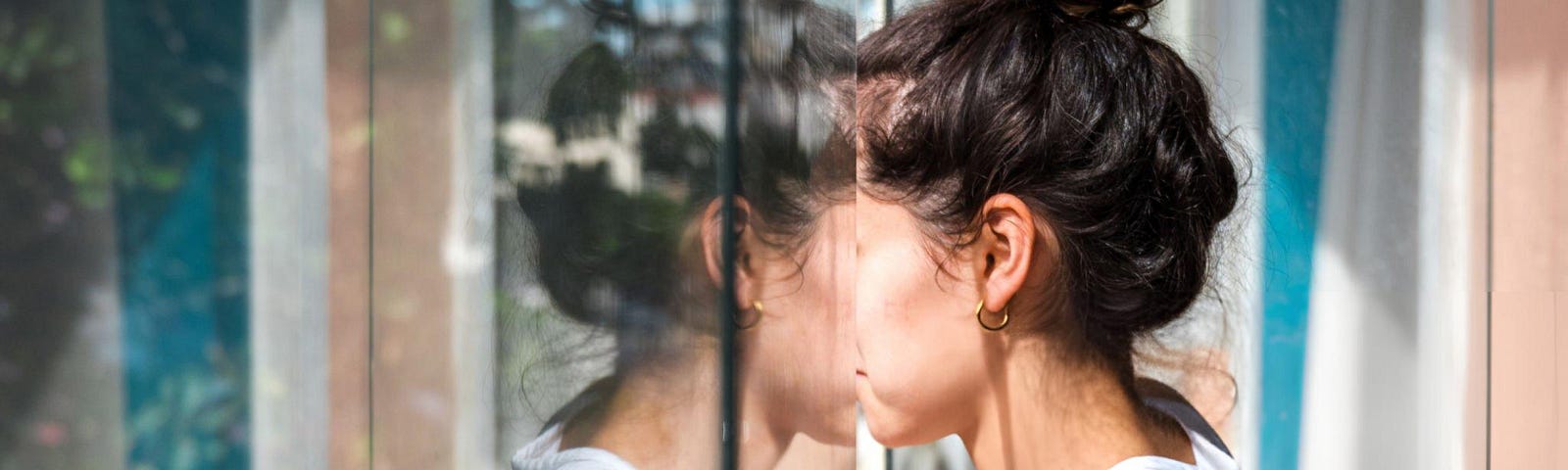 young woman looking out of window and reflecting in pane