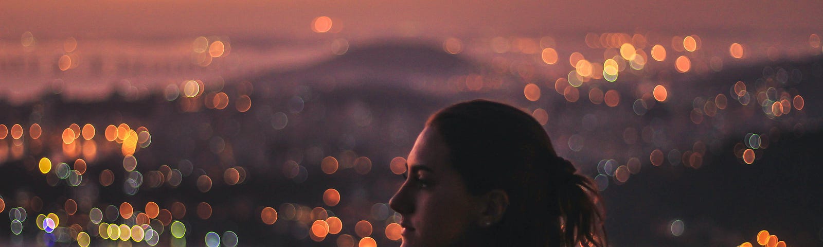 A woman looks out into the distance at sunrise. The city skyline is behind her.