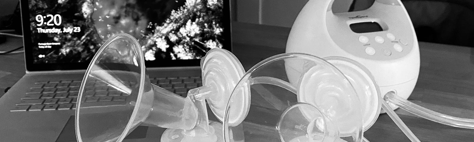 A breast pump machine sits on a desk in front of a laptop.