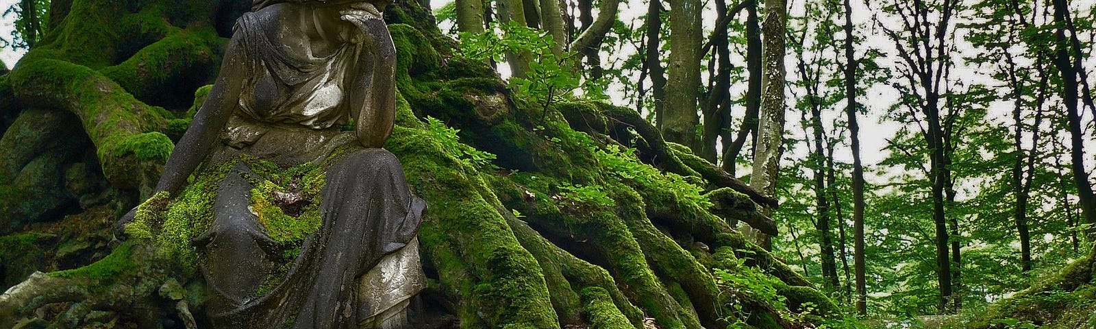 Roots covered in green moss with a weathered grey statue of a woman with her hand to her head among them.