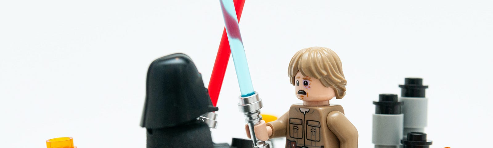 A lego Luke Skywalker fighting a lego Darth Vader with their light sabres. Luke looks unhappy.