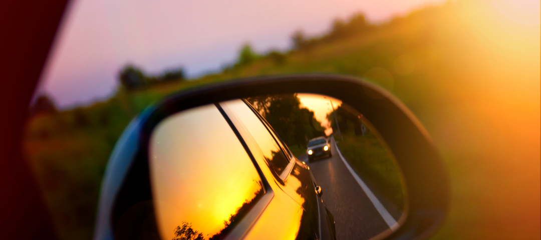 A side mirror on a car driving into the sunset
