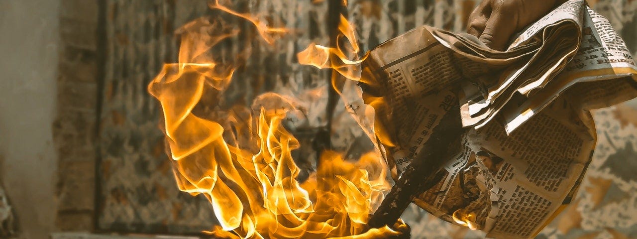 Person feeding newspaper into a dirty trashcan that is ablaze.