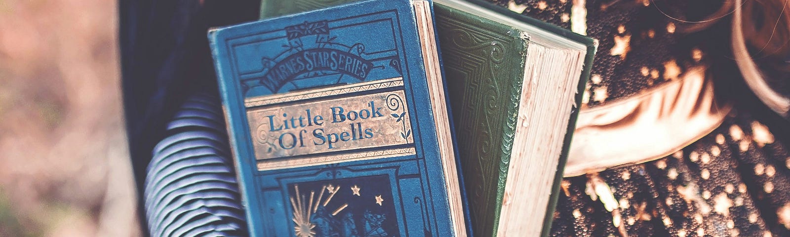 A woman holds two books, one is titled “Little Book Of Spells”