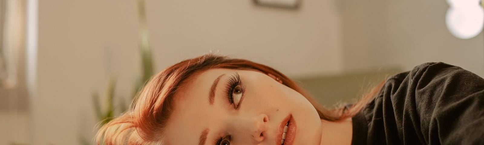 A red headed woman laying her head down on her arm on a glass table top reflecting upon something, as her image reflects back on herself.