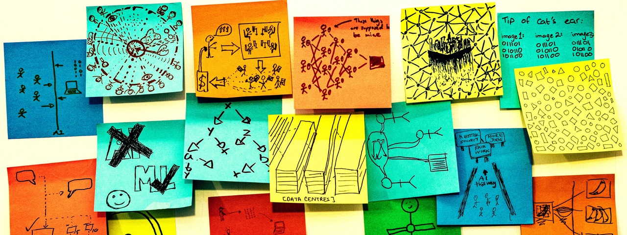 Seventeen multicoloured post-it notes are roughly positioned in a strip shape on a white board. Each one of them has a hand drawn sketch in pen on them, answering the prompt on one of the post-it notes “AI is….” The sketches are all very different, some are patterns representing data, some are cartoons, some show drawings of things like data centres, or stick figure drawings of the people involved.