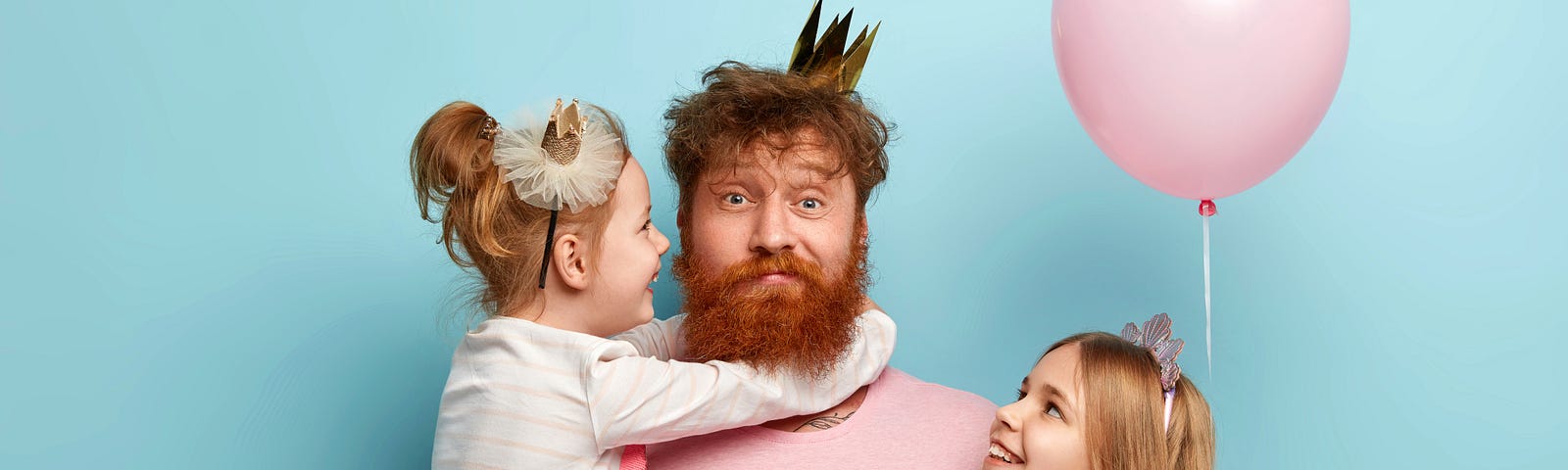 bearded dad holds two daughters, all wearing pink