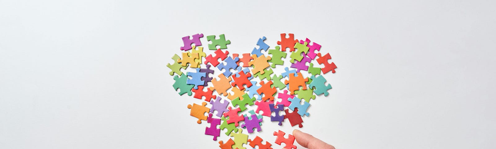 A hand placing a puzzle piece with other pieces that form a heart shape.