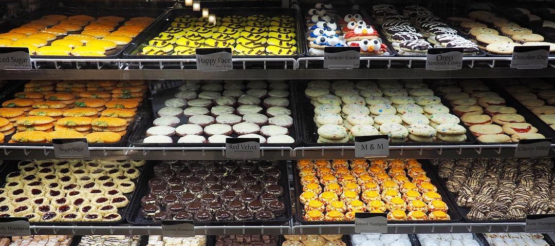 Shelves of cupcakes, cookies, and brownies on display for sale at a bakery.