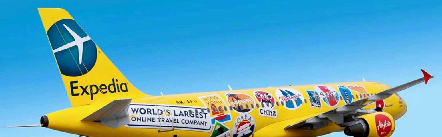 Yellow jet plane covered in travel stickers, flying through the sky