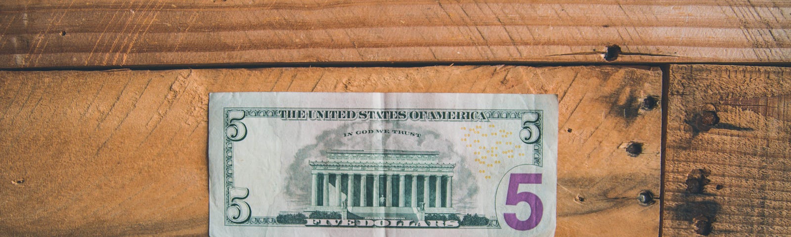 US 5 dollar bill lying on wooden floorboards.