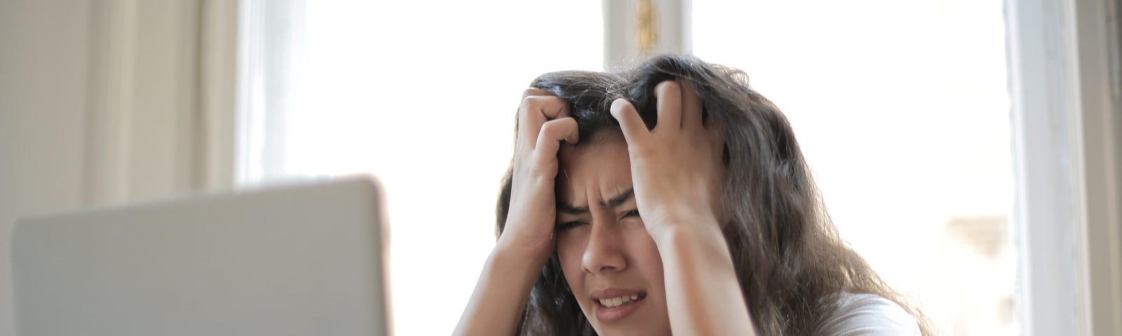 Woman wearing white blouse sitting in front of a laptop showing frustration.