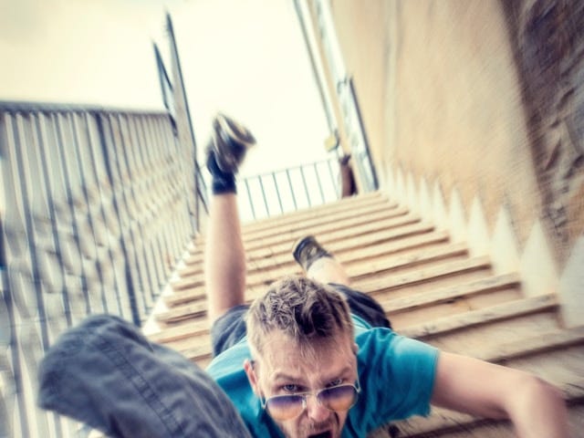 Photo of a young man falling headlong down a flight of stairs. He is wearing sunglasses and a blue T-shirt.