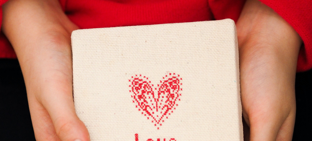 hands holding cross stitch piece that says love