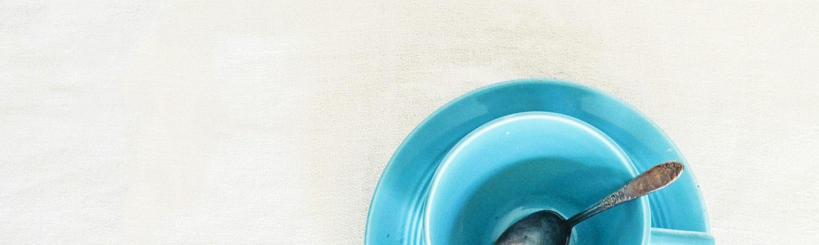 Blue tea cup on a blue saucer with a metal spoon.