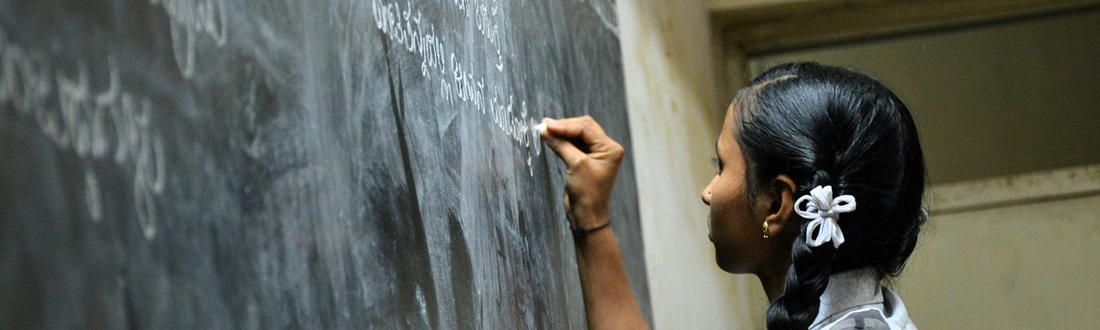 A young girl is writing on the blackboard in class.