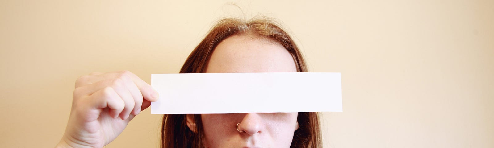Woman wearing red shirt covers her eyes with a plain white paper.