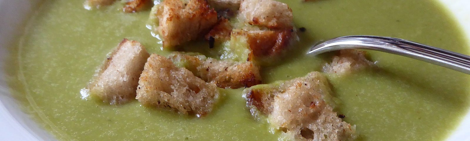 Croutons rest in a bowl of pea soup.