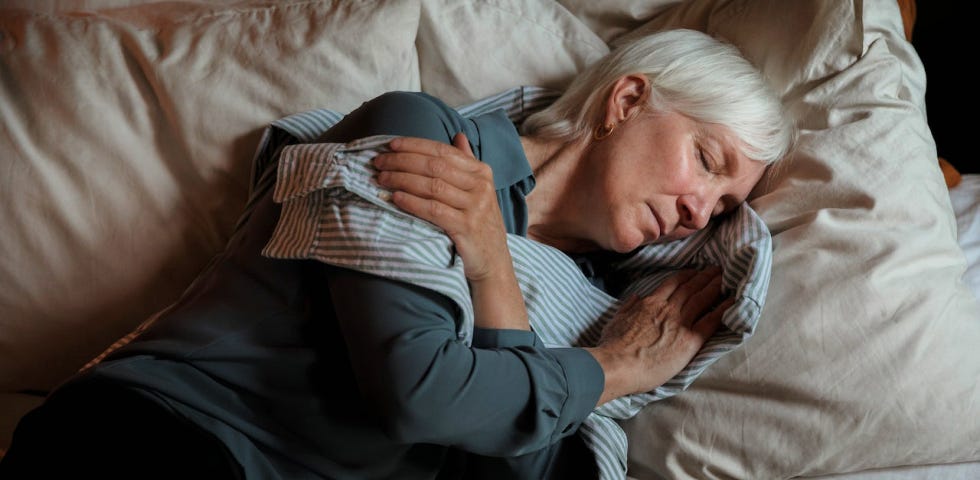 An older woman holding a shirt to her chest and sleeping.