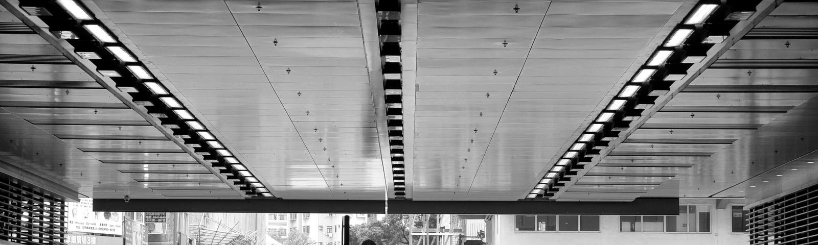 Black & White photo of the coverage of metal ceiling with illumination, viewing to the street far opposite.