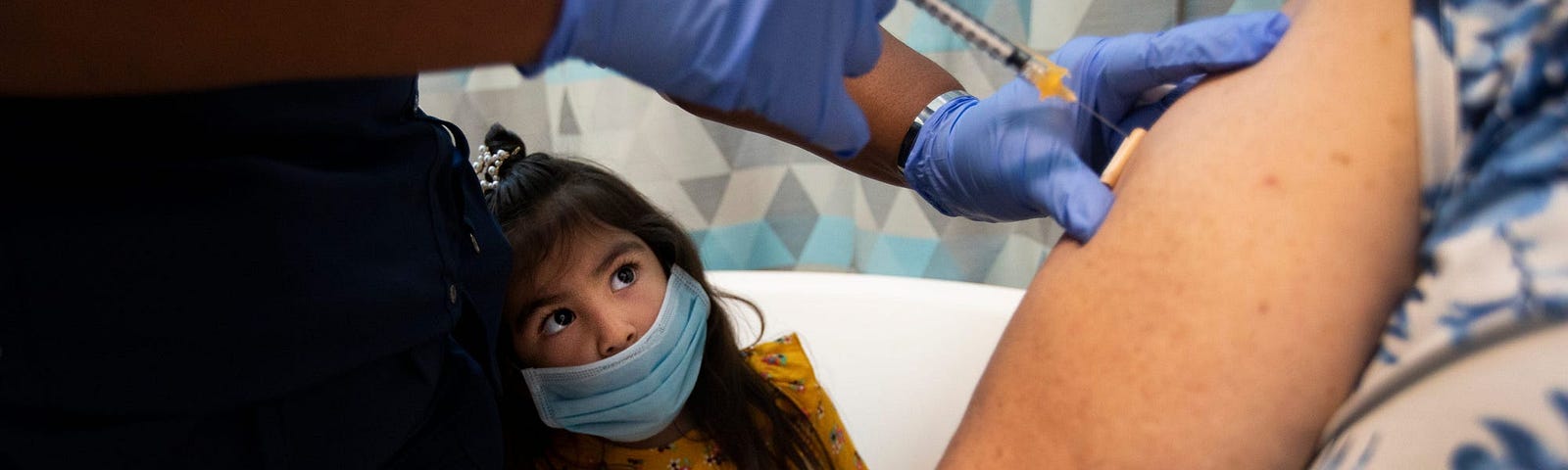 A child watches an individual receive a coronavirus vaccine.