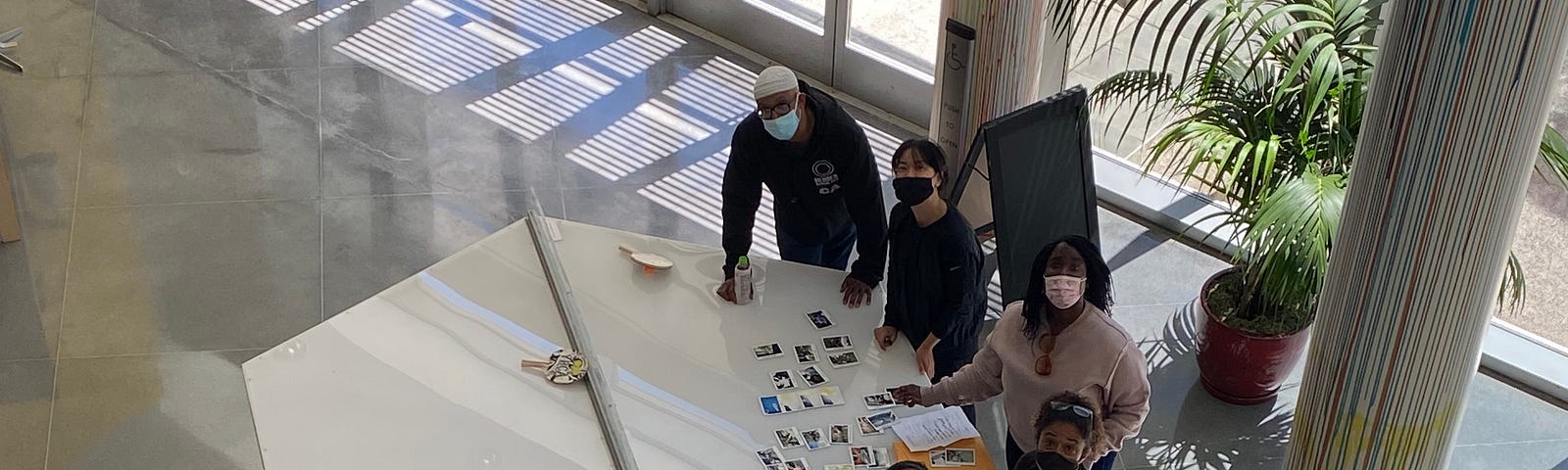 Bird’s eye view of five artists looking up for a photo. They are sorting photos on a table with natural light streaming in from the large windows behind them.