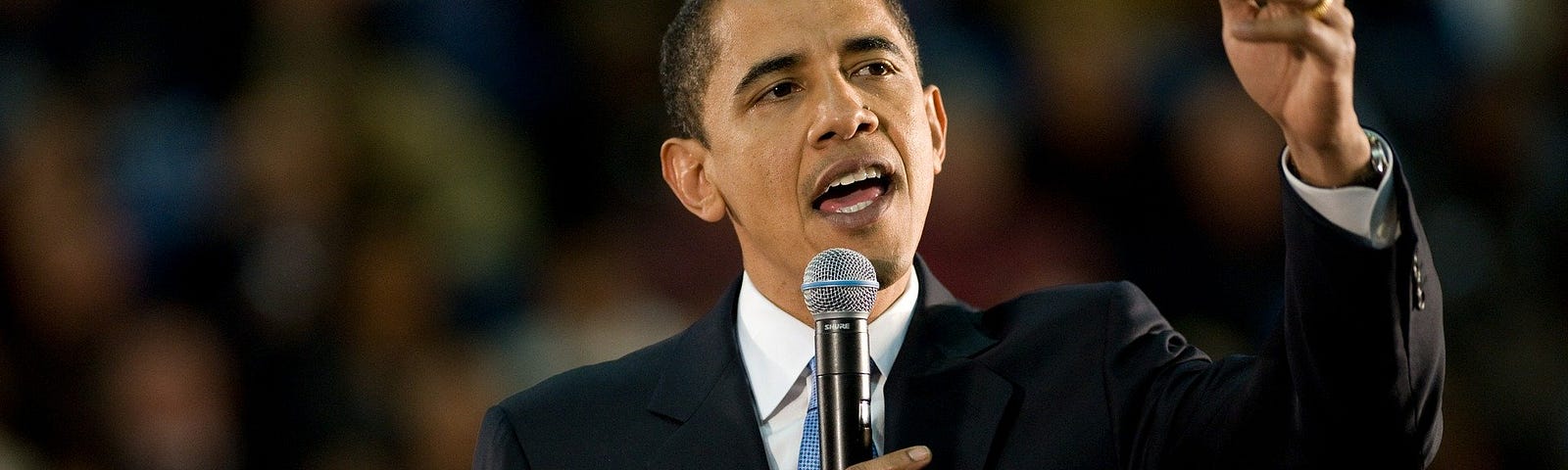 President Obama holds up microphone while delivering remarks to crowd.